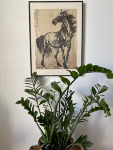 Peinture traditionnelle asiatique représentant un cheval noir encadrée au mur avec plante verte en pot dans l’entrée du Château Papounan, chambre d’hôtes de charme à Saint-Estèphe, Médoc.