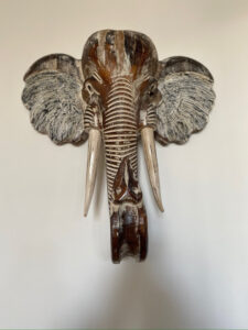 Tête d’éléphant sculptée en bois avec finitions patinées accrochée au mur dans l’entrée du Château Papounan, chambre d’hôtes de charme à Saint-Estèphe, Médoc.