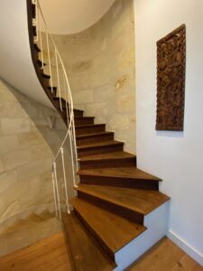 Escalier en bois massif avec rampe blanche et sculpture murale asiatique en bois dans l’entrée du Château Papounan, chambre d’hôtes de charme à Saint-Estèphe, Médoc.
