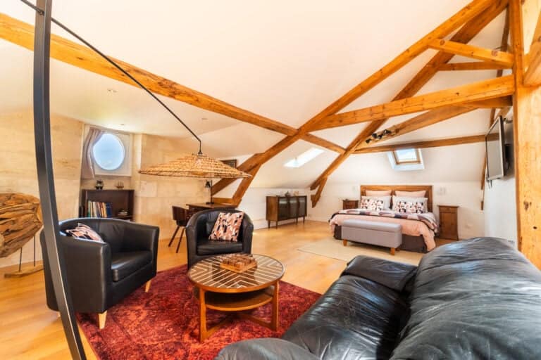 Vue intérieure de la Suite l’Estuaire avec lit queen-size, coin salon, poutres apparentes et décoration raffinée au Château Papounan, chambre d’hôtes de charme à Saint-Estèphe, Médoc.
